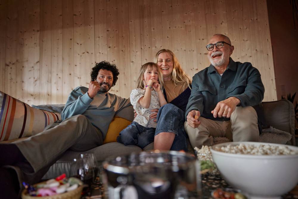 Glad familj tillsammans i soffan ser på tv med skål popcorn.